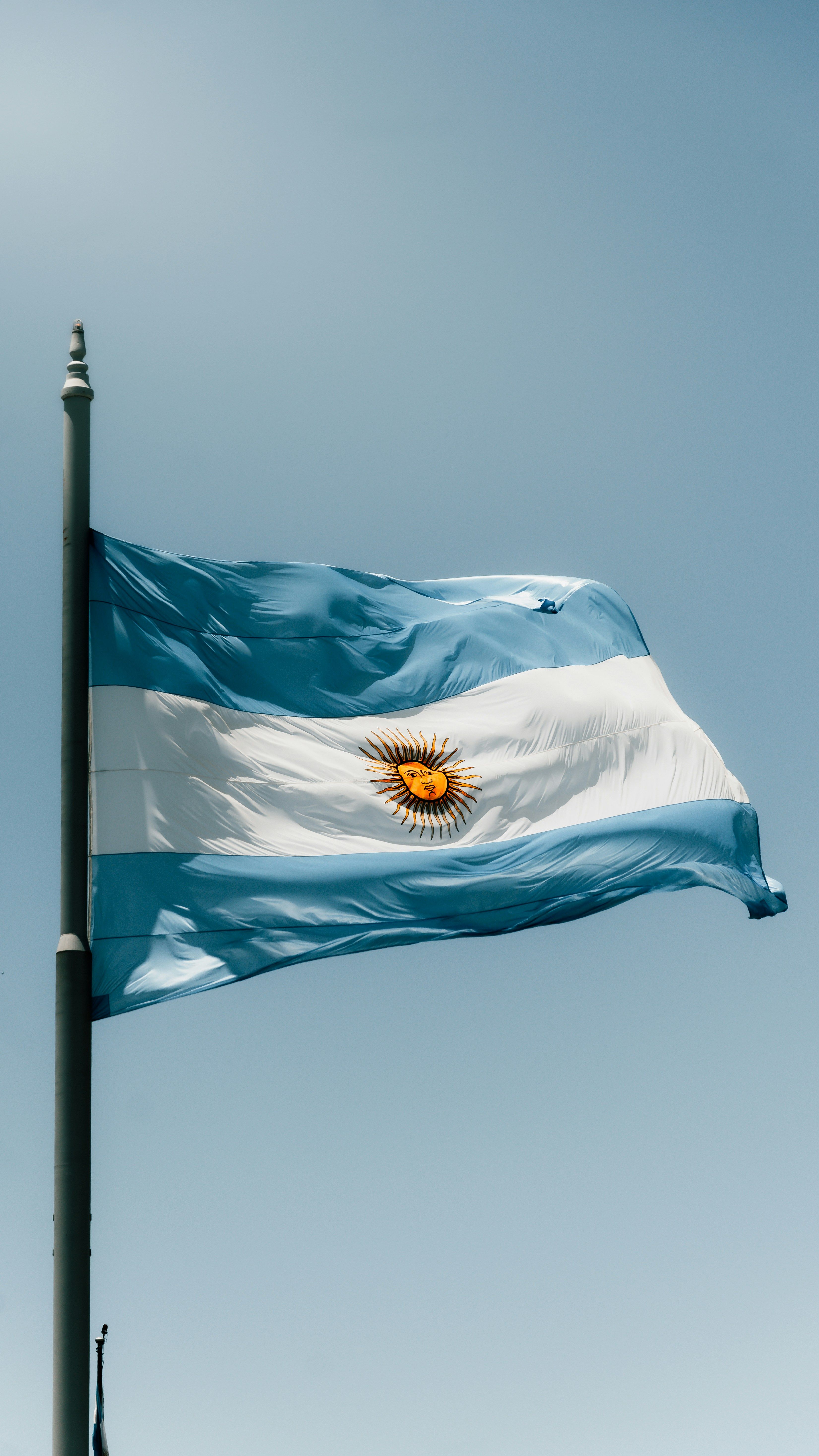 Argentinian flag waving on a pole against a bright blue sky, showcasing national pride.