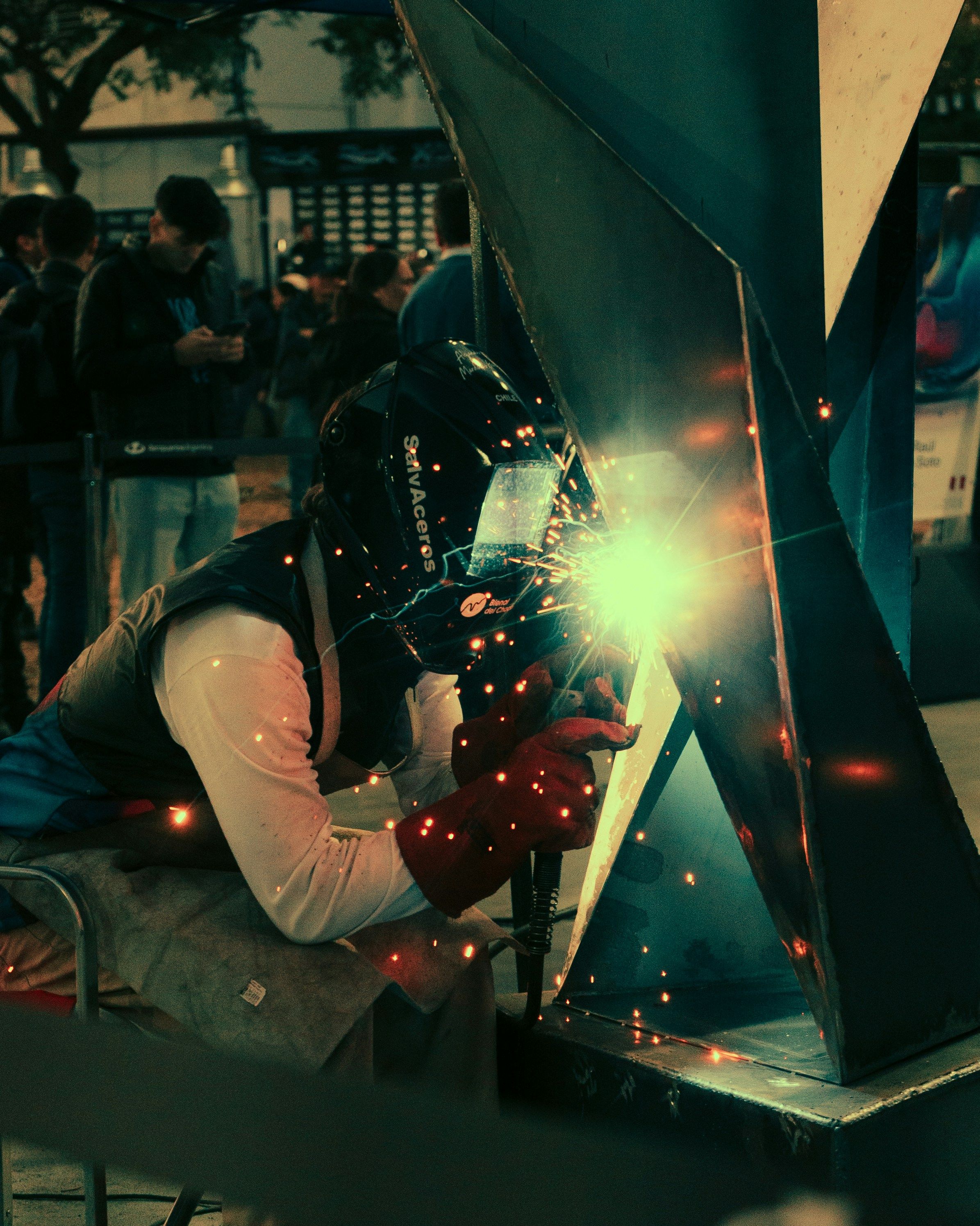A welder with helmet performs skilled metalwork indoors, sparks flying.