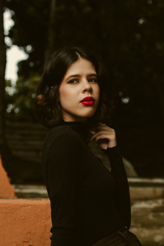 Portrait of a fashionable woman with striking red lipstick against an outdoor backdrop.