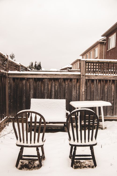 Free Serene winter scene with empty snow-covered chairs and table in a backyard. Stock Photo