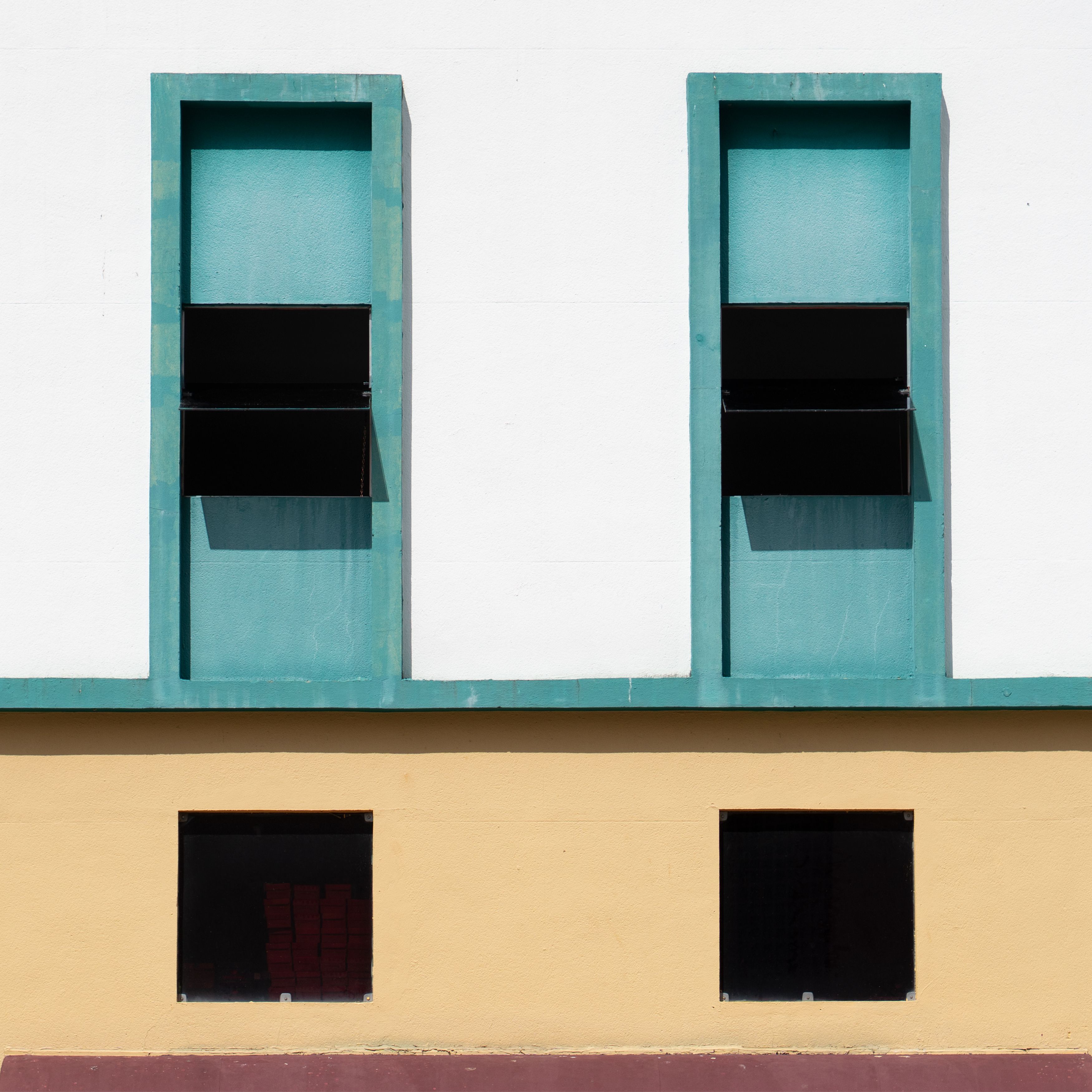 Minimalist facade with two teal windows and yellow accents showcasing architectural symmetry.