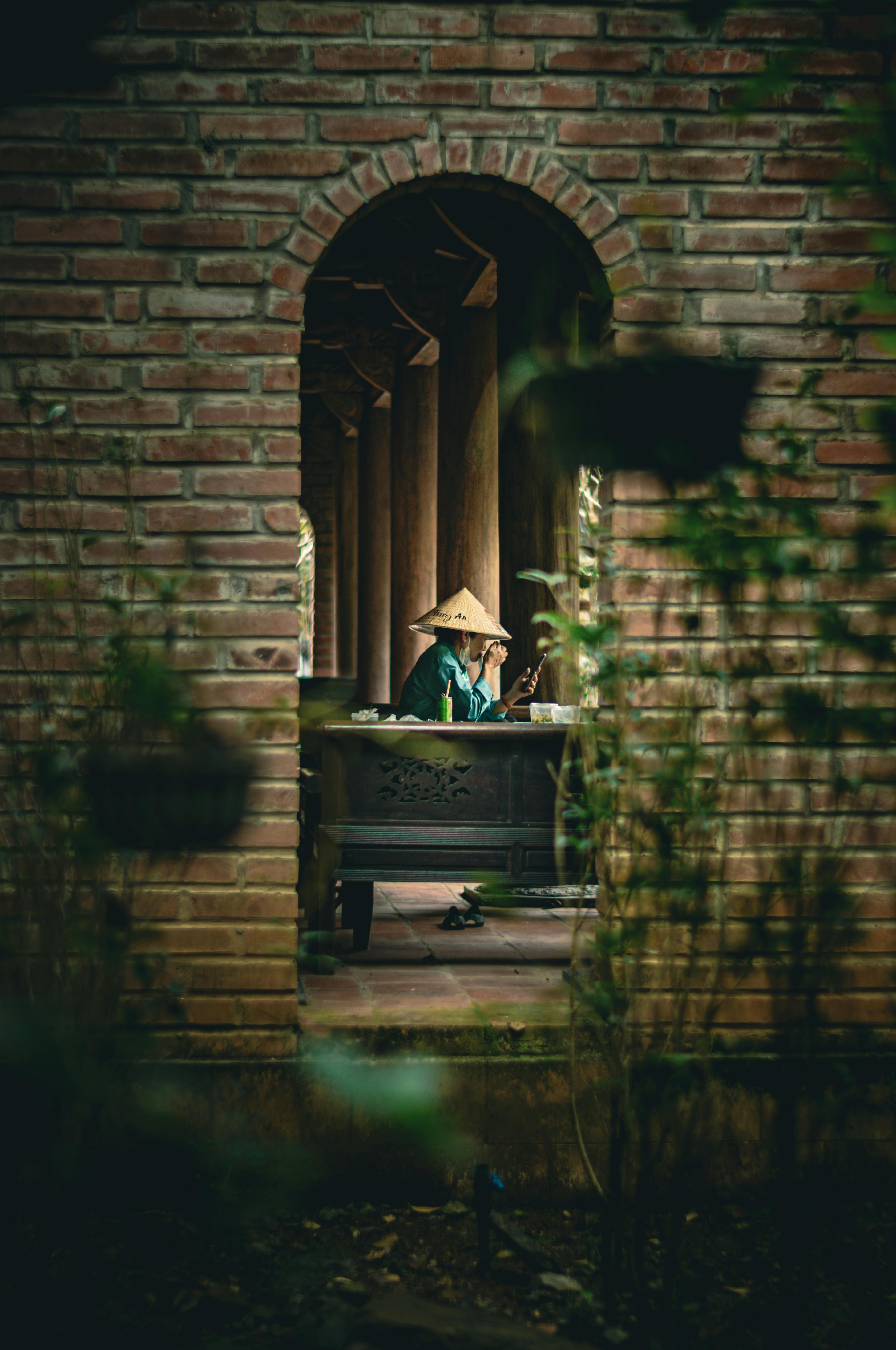 A person in traditional attire viewed through a brick archway in Ninh Bình, Vietnam.