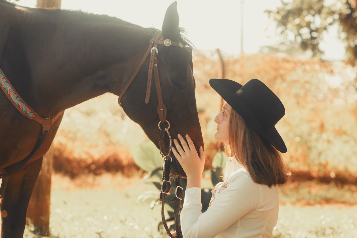 Cow-girl en chapeau noir caressant son cheval dans un pré baigné de lumière