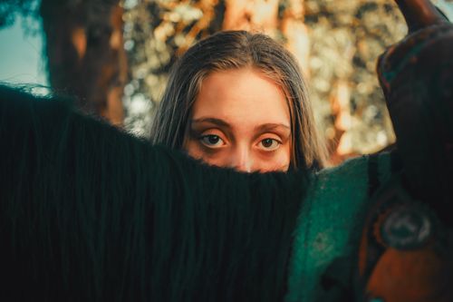 Free Portrait of a woman partially hidden by a horse's mane in an outdoor setting, conveying mystery and connection. Stock Photo
