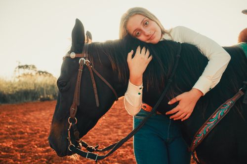 Free A young woman lovingly embraces a horse outdoors during a warm sunset. Stock Photo
