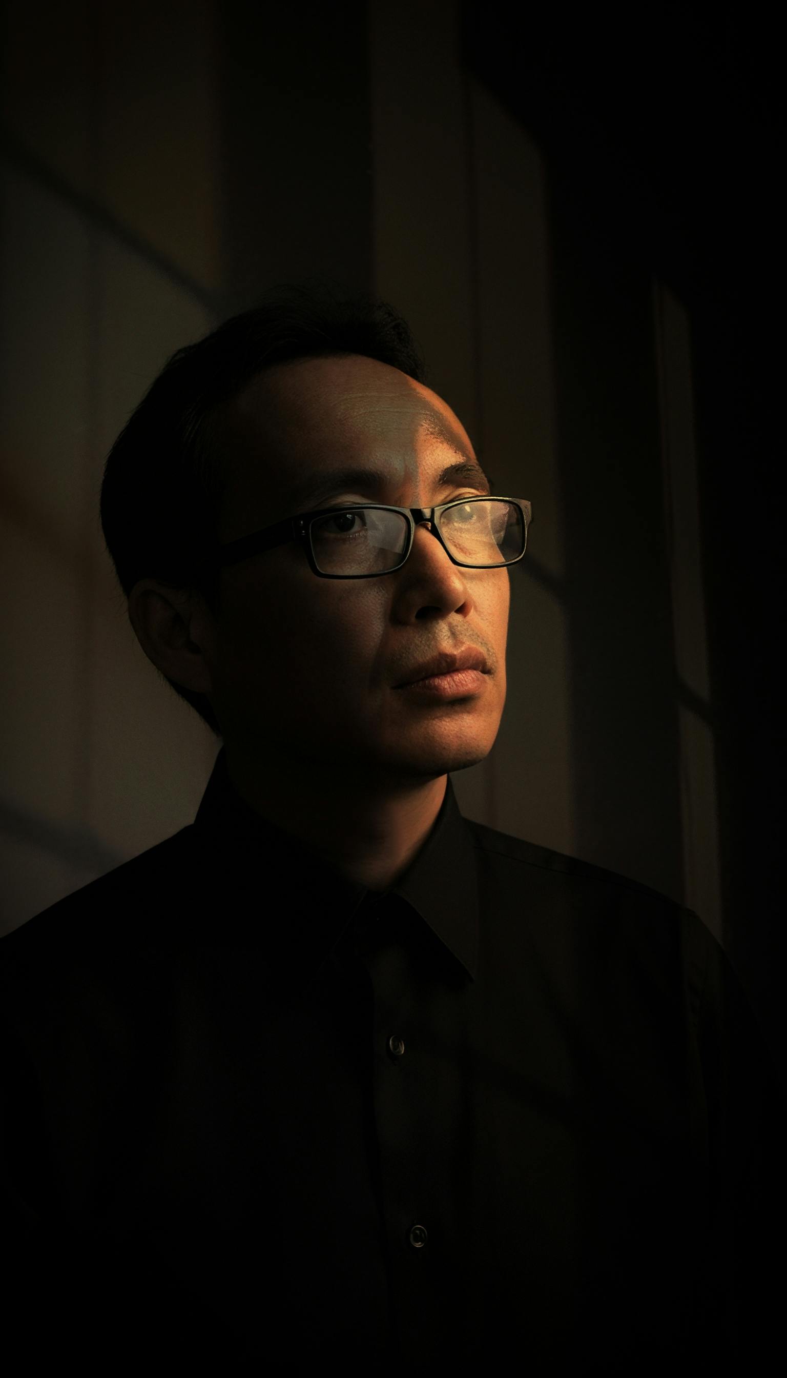 Moody portrait of a man in glasses, capturing thoughtful introspection.