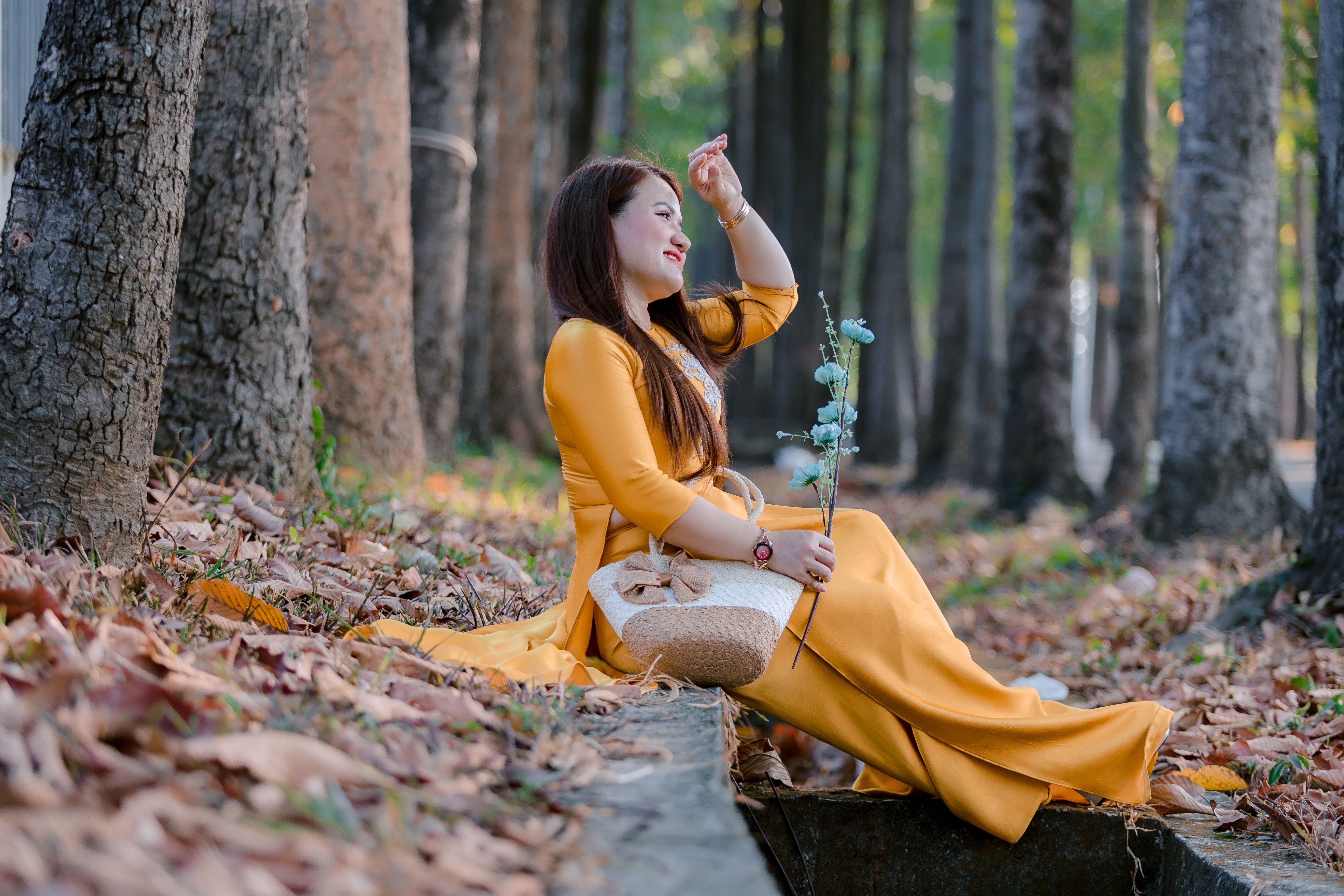 A woman in a yellow dress, sitting with a flower in a serene forest setting.
