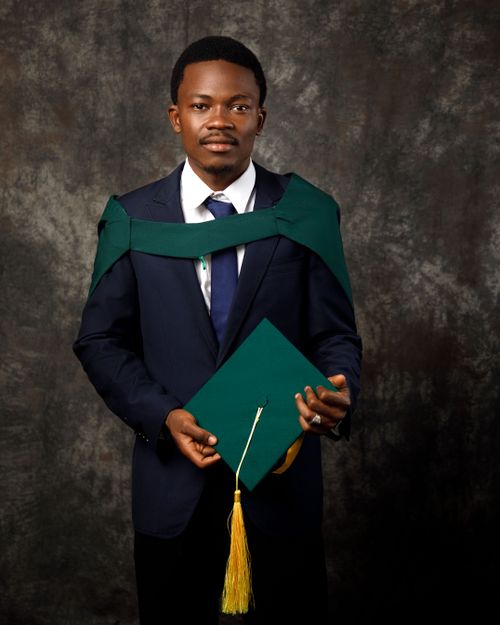 Free Young graduate in formal attire holding certificate against dark backdrop. Stock Photo