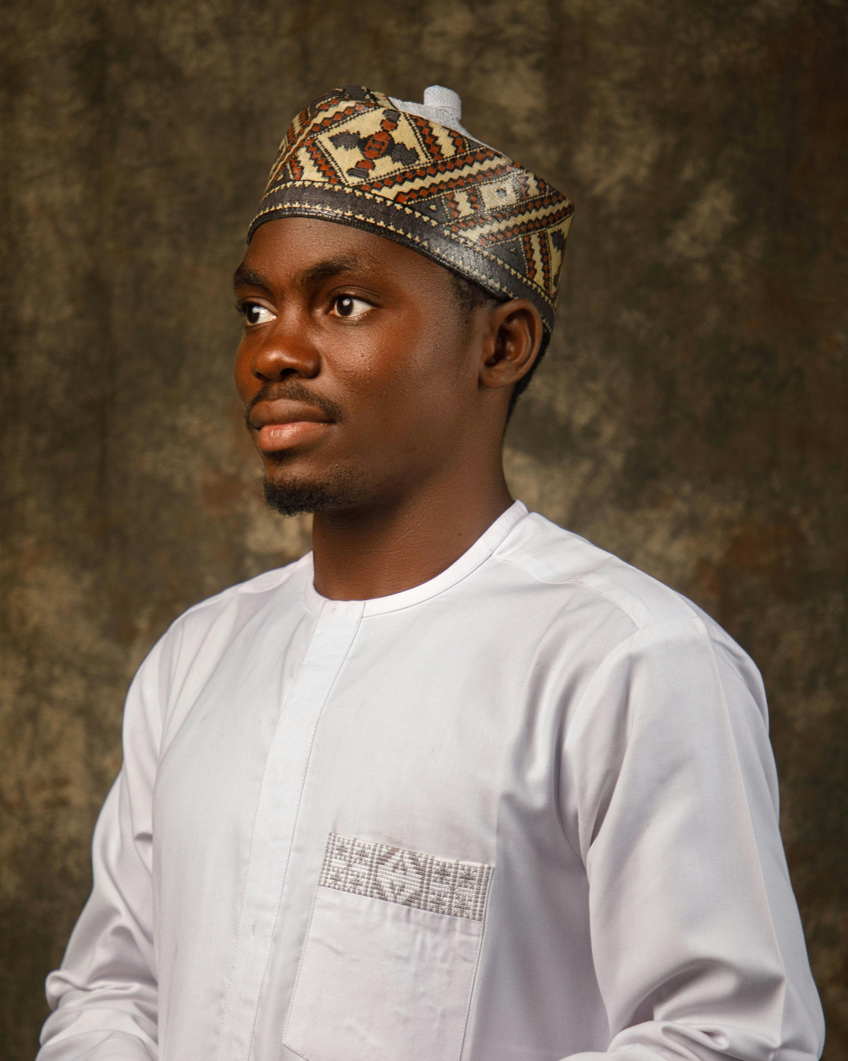 Portrait of a man in traditional attire and embroidered cap against a textured background.