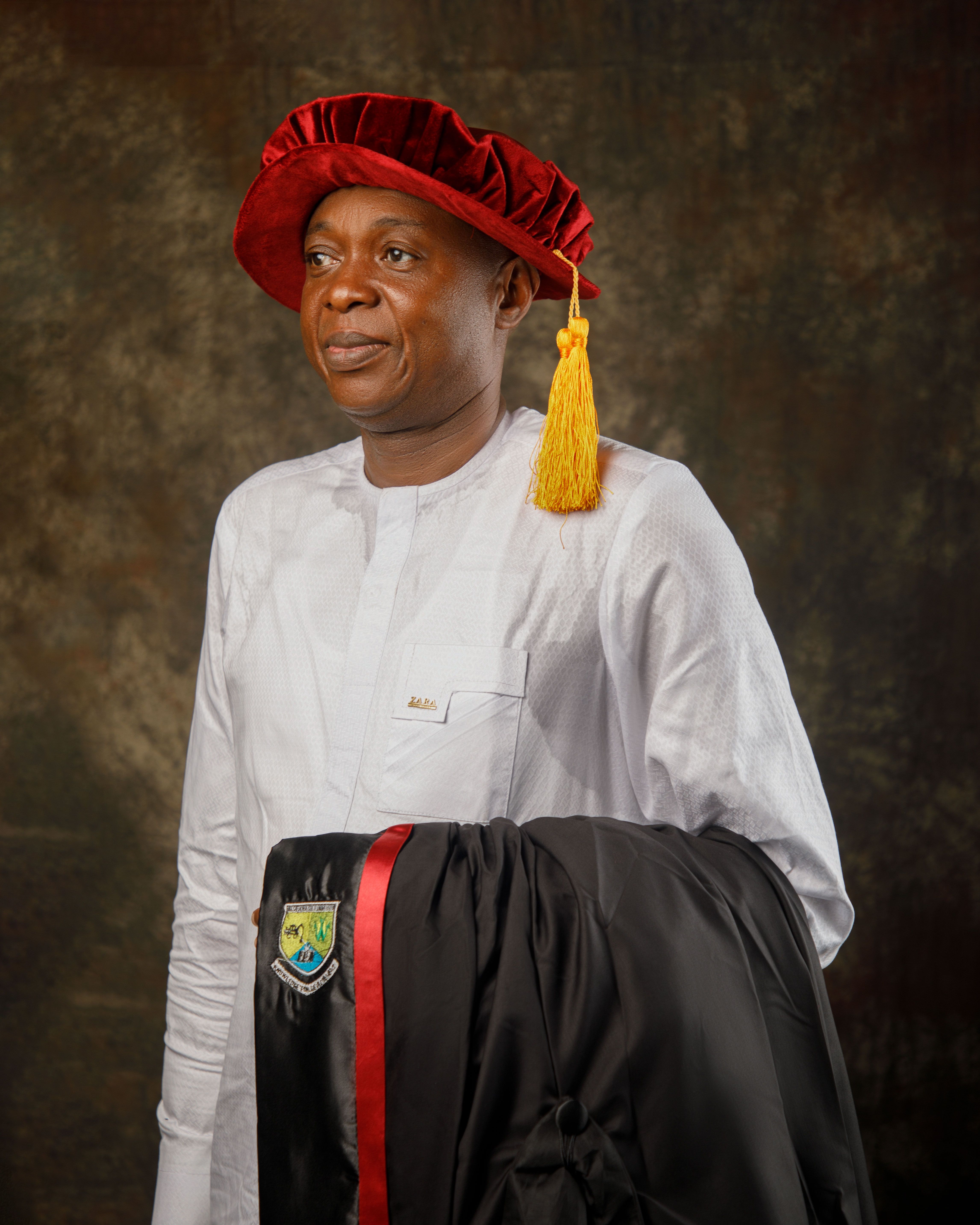 Man in academic regalia posing for a graduation portrait with a ceremonial cap.