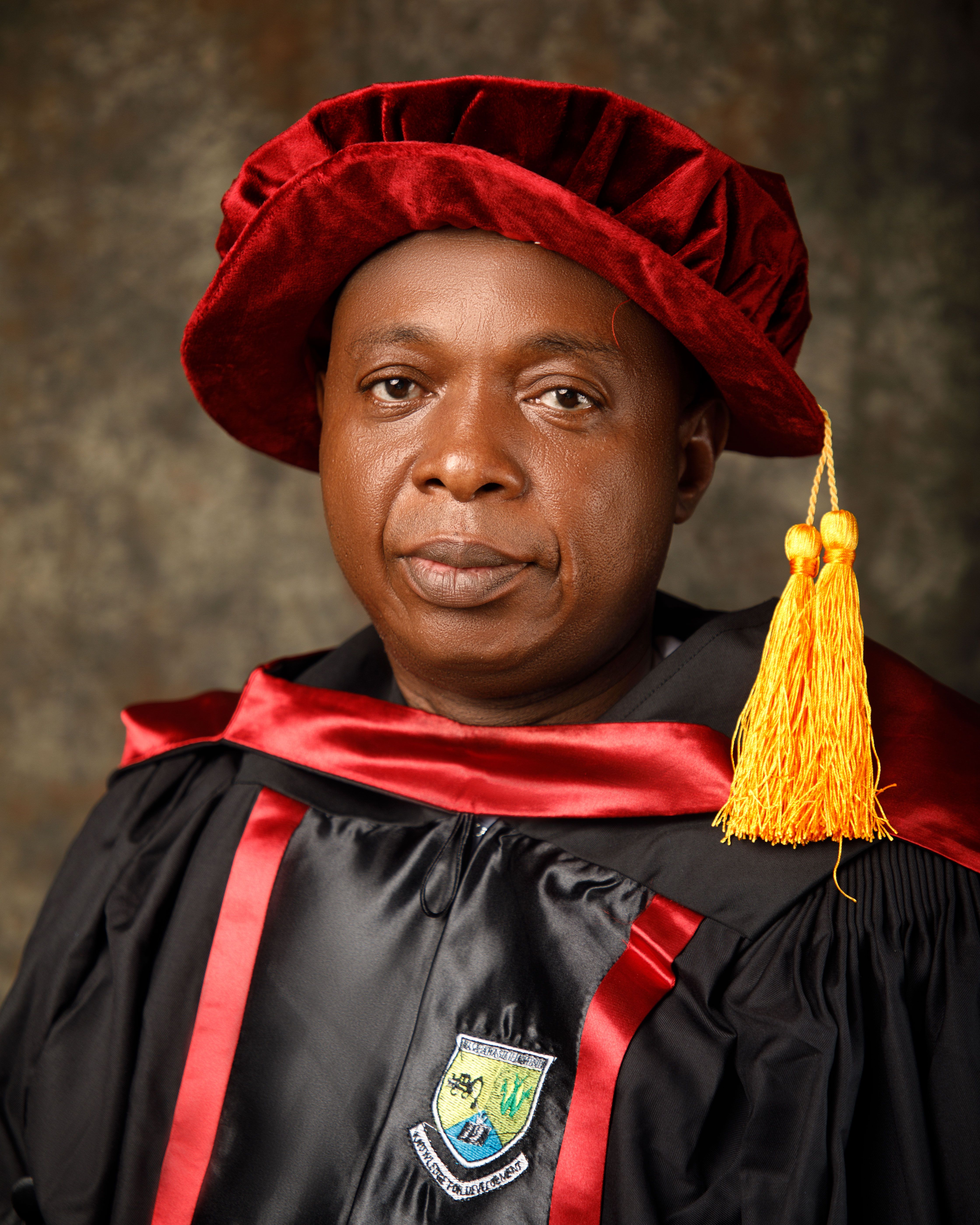 Formal portrait of an African academic wearing red and black graduation regalia with tassel.