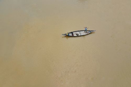 Free Drone footage of a single boat floating on a calm river in Bangladesh, showcasing serenity and simple lifestyle. Stock Photo