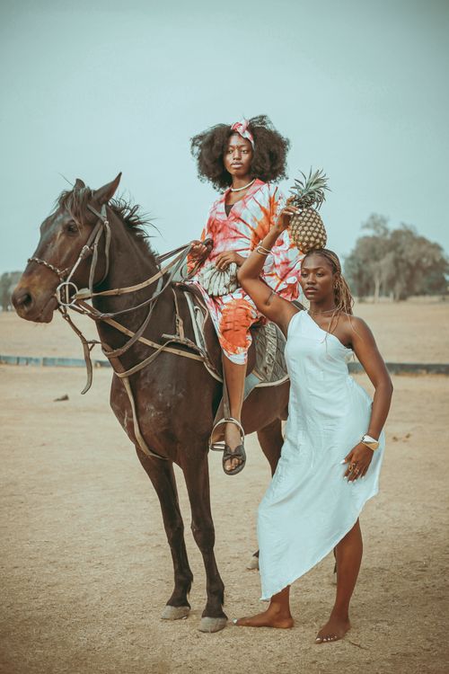 Free Two vibrant women in colorful attire pose confidently with a horse outdoors. Stock Photo