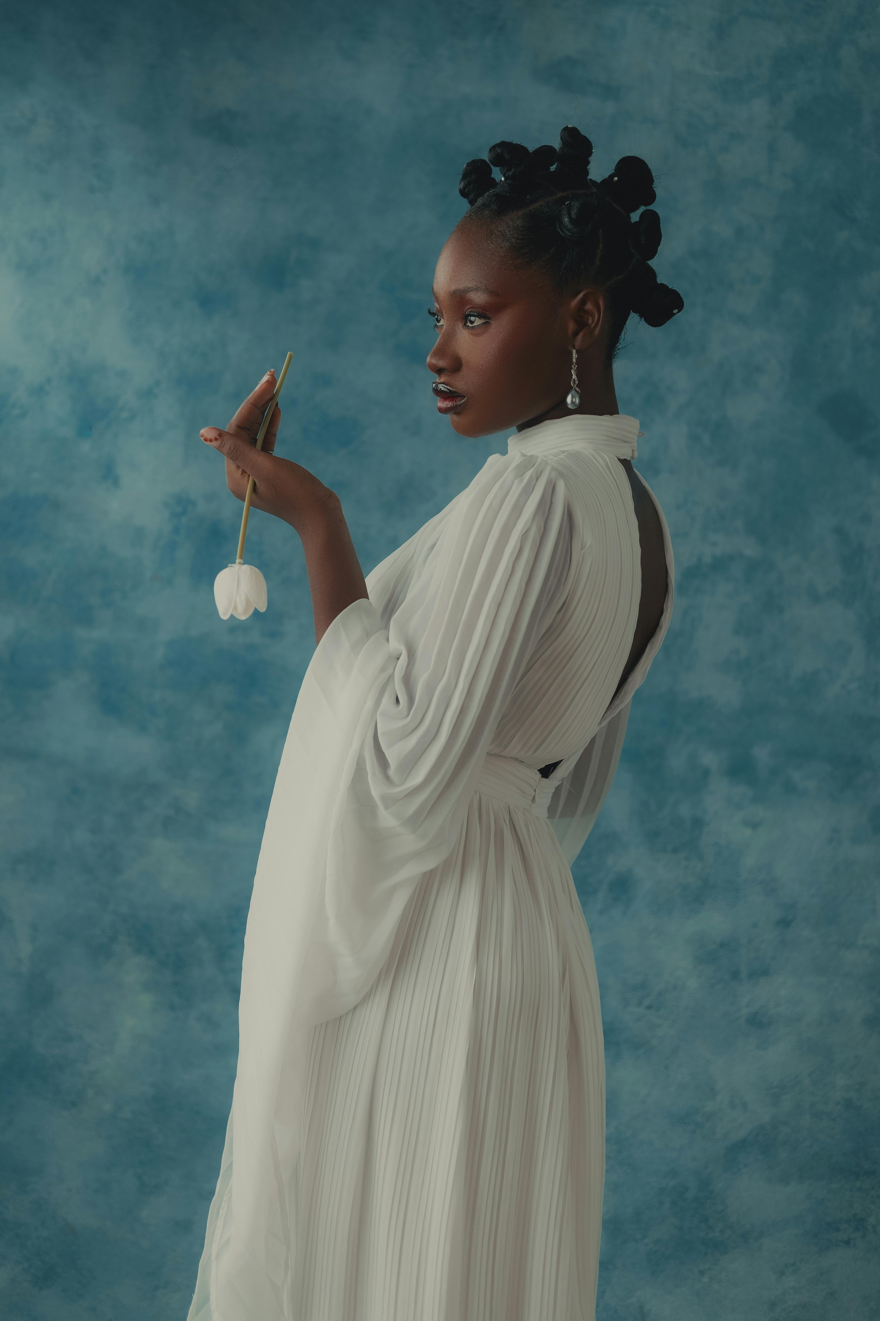 Portrait of a graceful African woman with traditional hairstyle in white dress holding a flower.