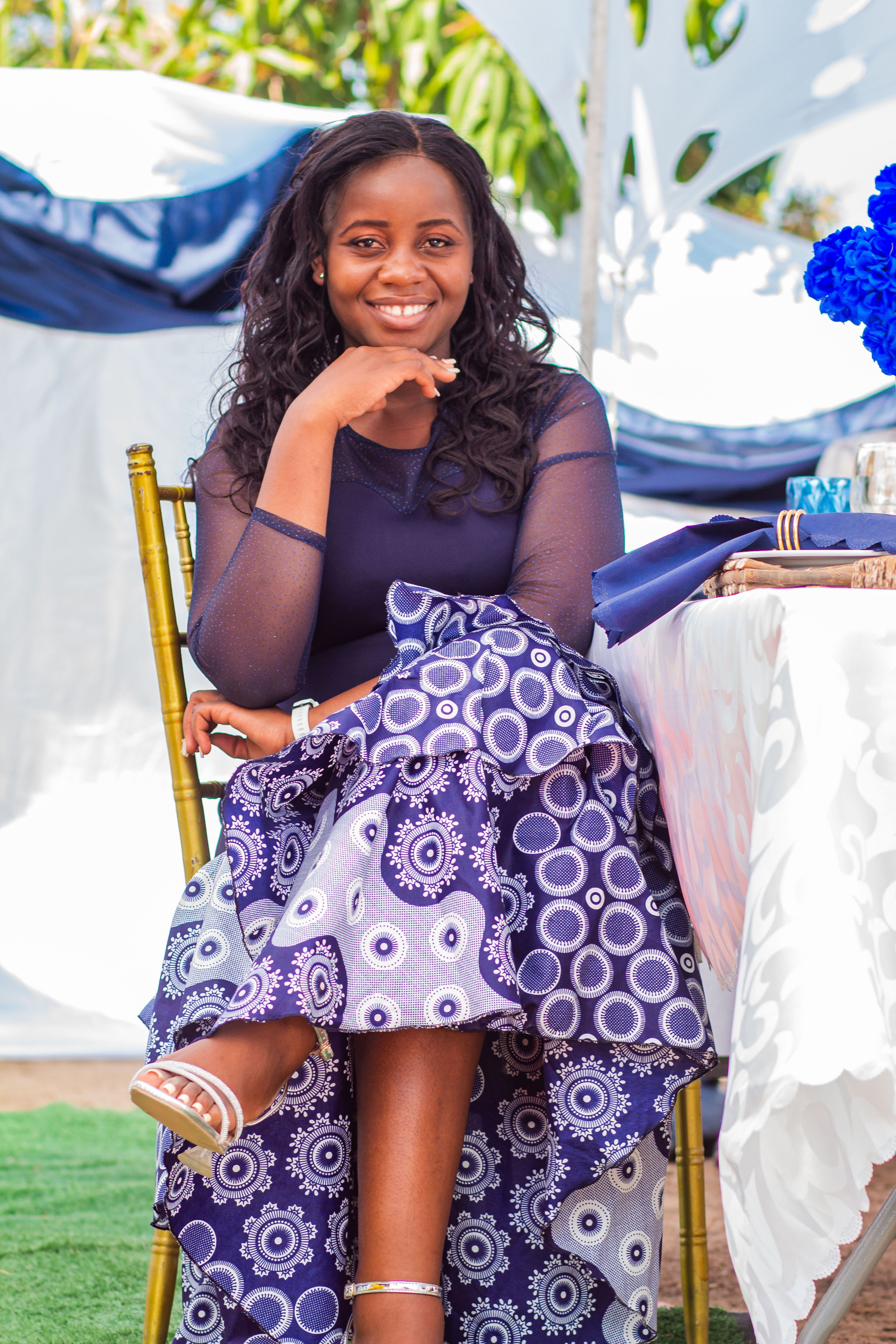 Mulher alegre em um vestido azul e branco sentada em uma mesa decorada de evento ao ar livre.