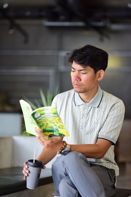 Free Young man sipping coffee while reading a book in a contemporary indoor cafe. Stock Photo