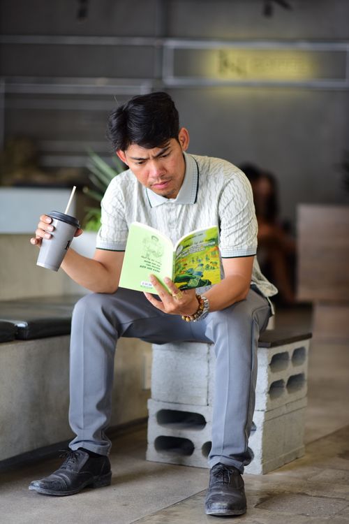 Free Focused man reading a book while enjoying a beverage in a casual setting. Stock Photo