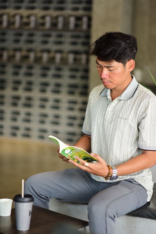 Free Man reading a book indoors with a drink in a relaxed setting, featuring comfy attire. Stock Photo
