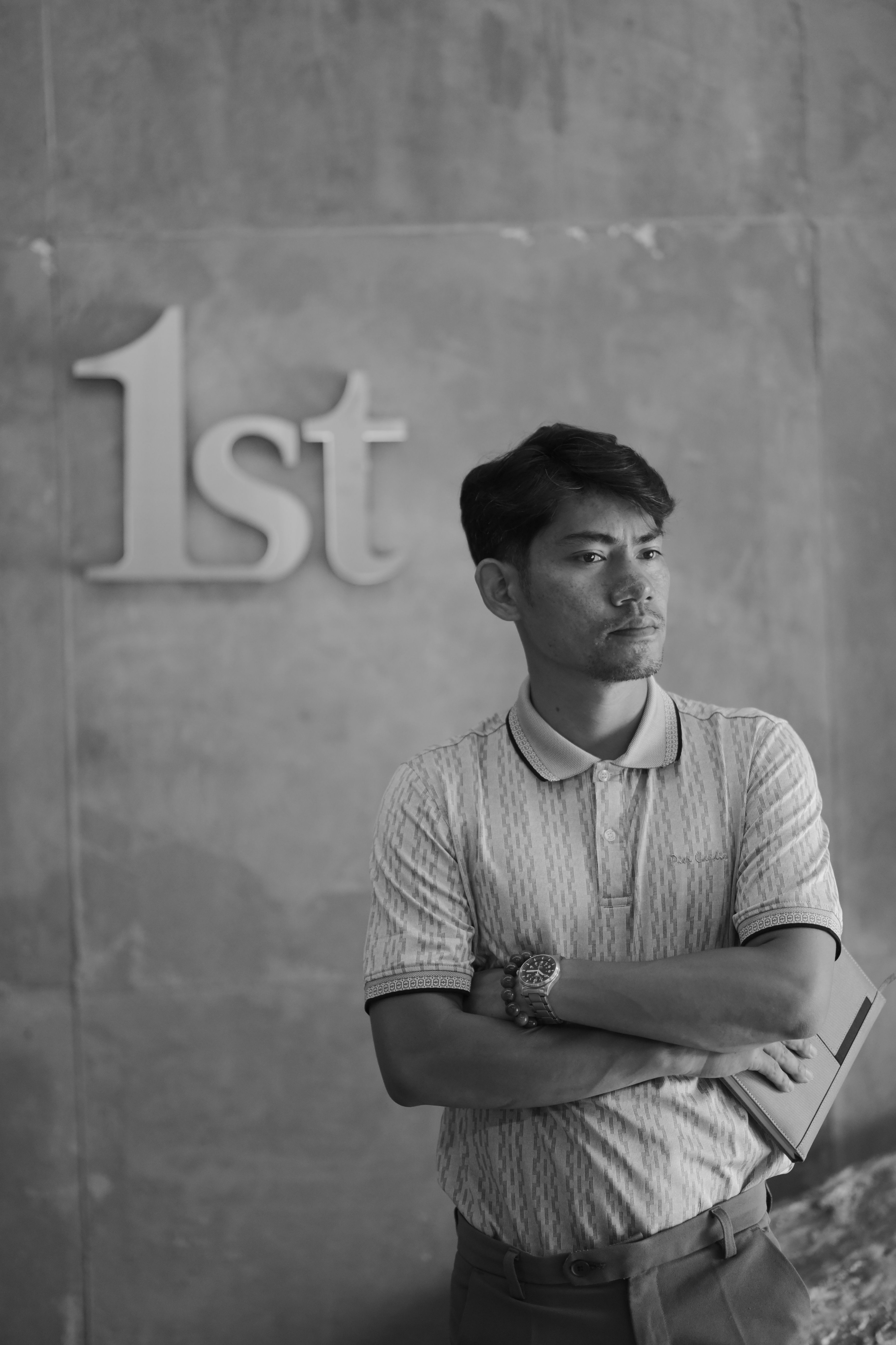 Thoughtful man in monochrome, leaning on a wall with '1st' sign, conveying contemplation.