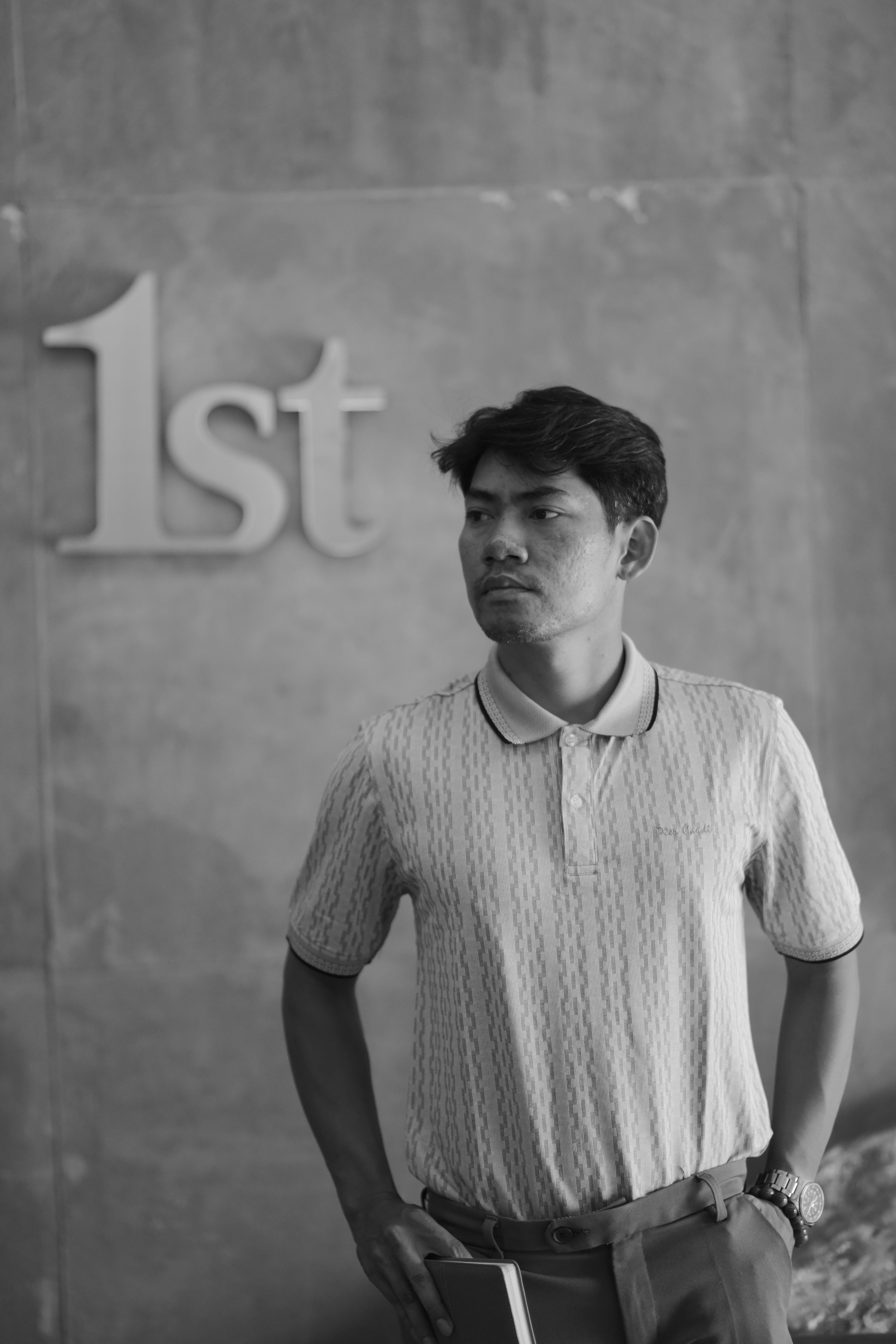 Black and white portrait of a thoughtful man with '1st' sign in the background.