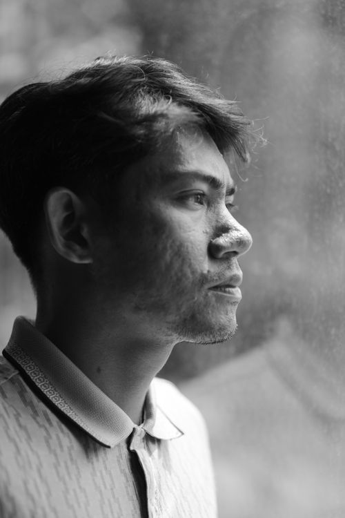 Free Black and white portrait of a man looking out of a window, creating a reflective mood. Stock Photo