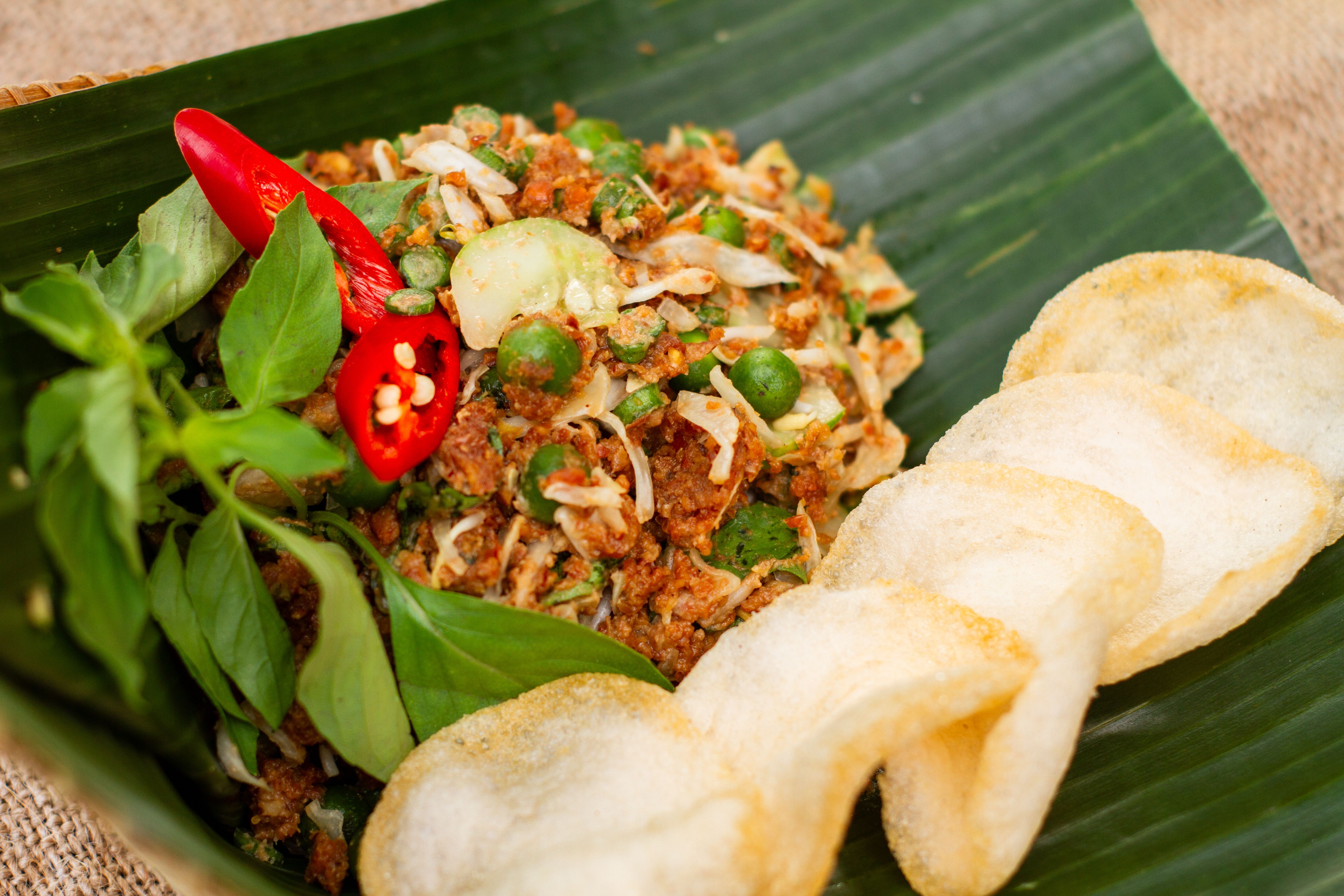 Traditional Thai larb served on a banana leaf with fresh herbs, lime wedges, and small red chilies visible