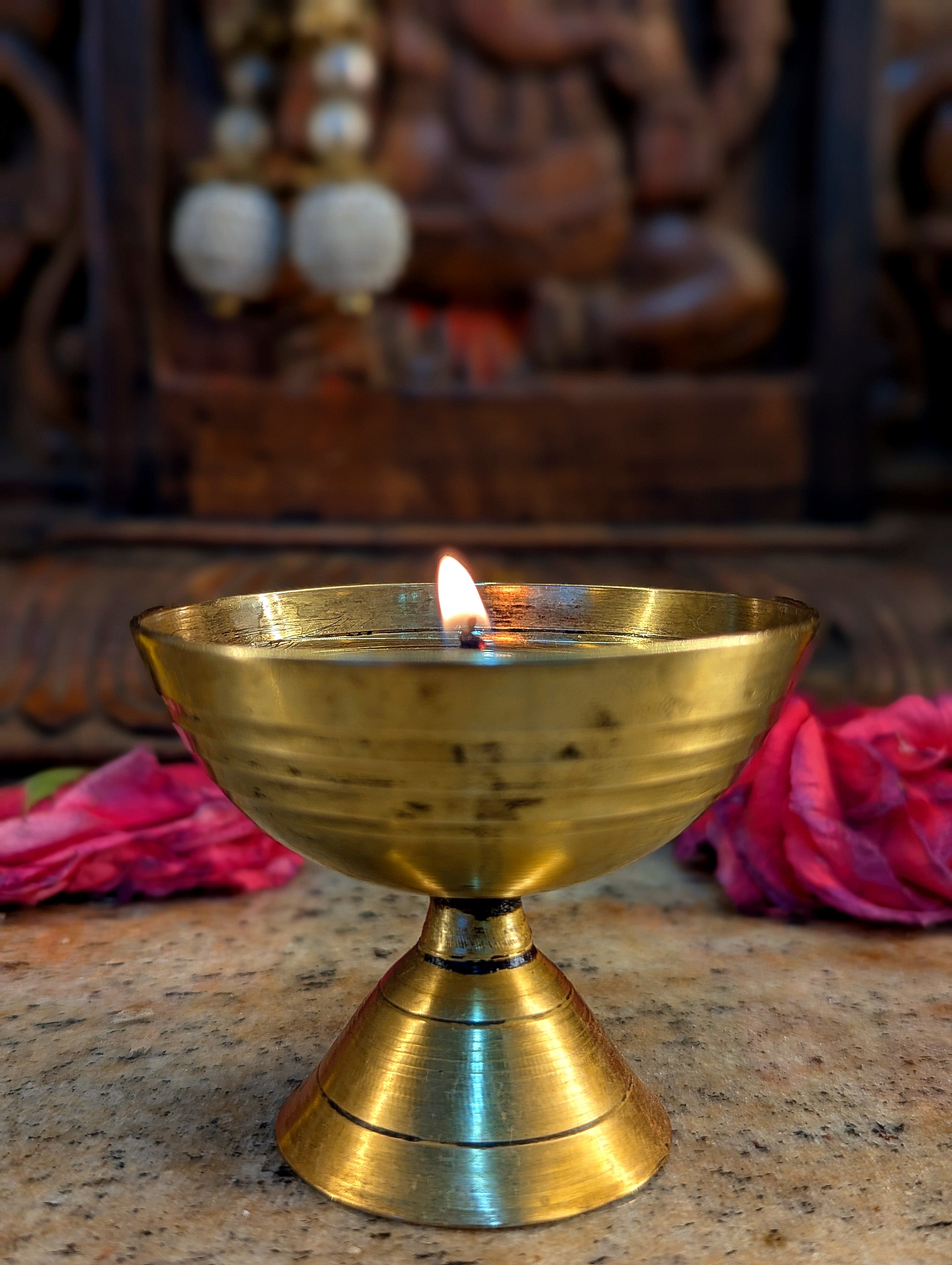 Brass oil lamp with flame, adorned by rose petals, creating a serene and spiritual ambiance.