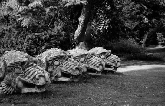 Monochrome photo of four stone dragon head sculptures on grass in a park setting.