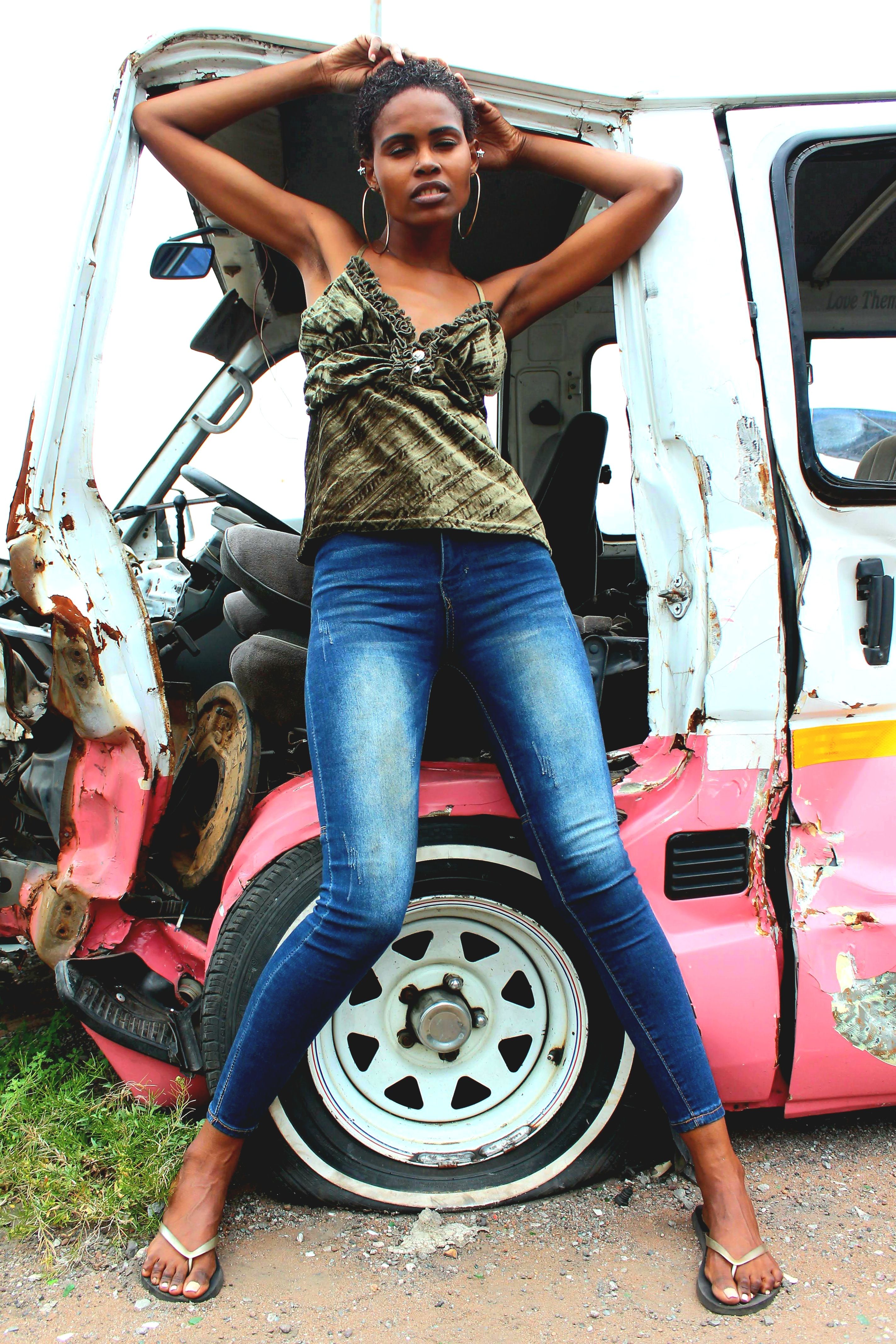Confident woman poses against a rusted vehicle, embracing urban style in South Africa.