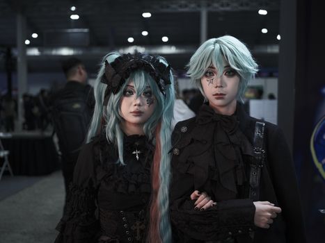 Two adults in elaborate goth-inspired cosplay costumes at an indoor convention.