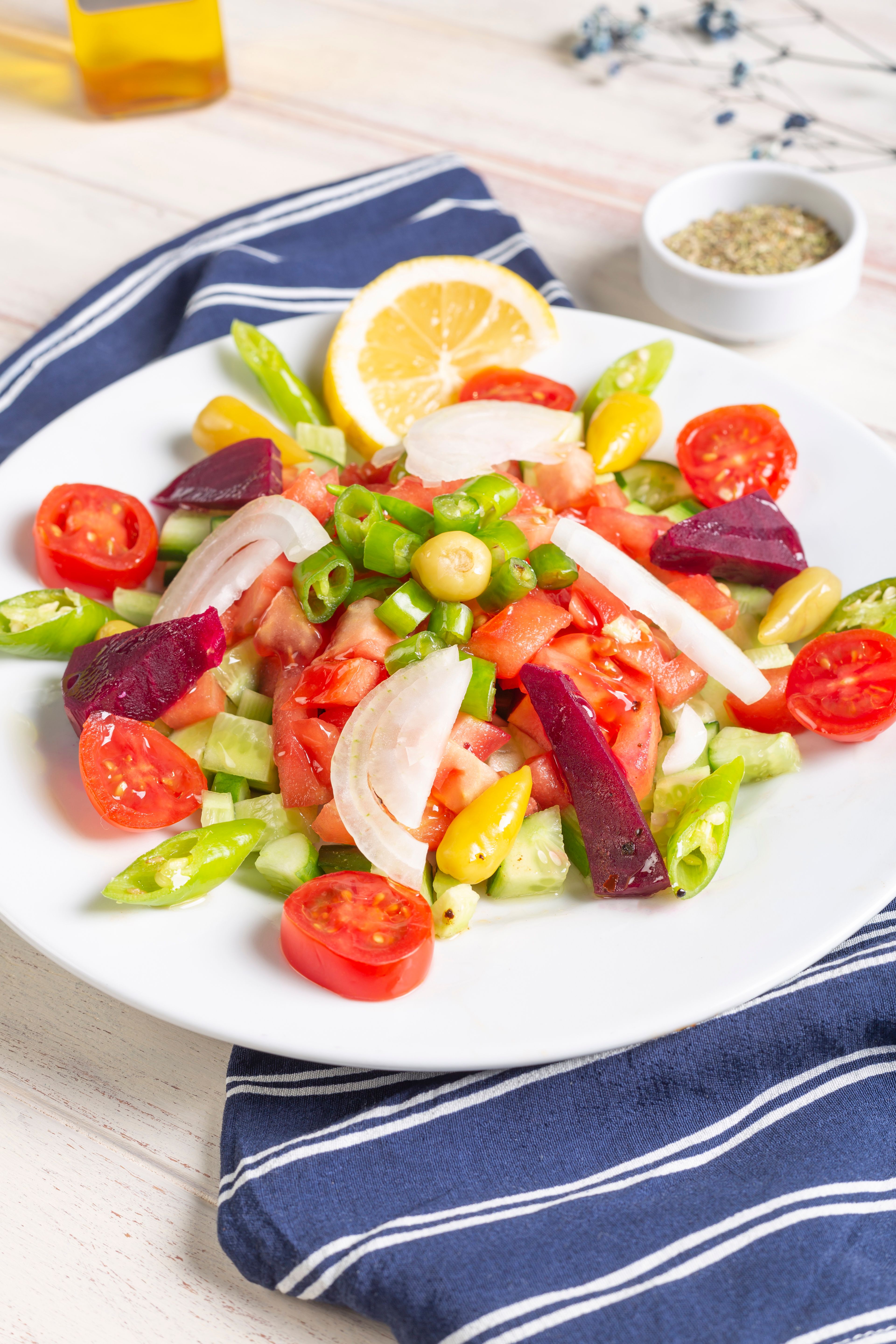 A vibrant Mediterranean salad with cherry tomatoes, cucumbers, olives, and lemon slice on a white plate.