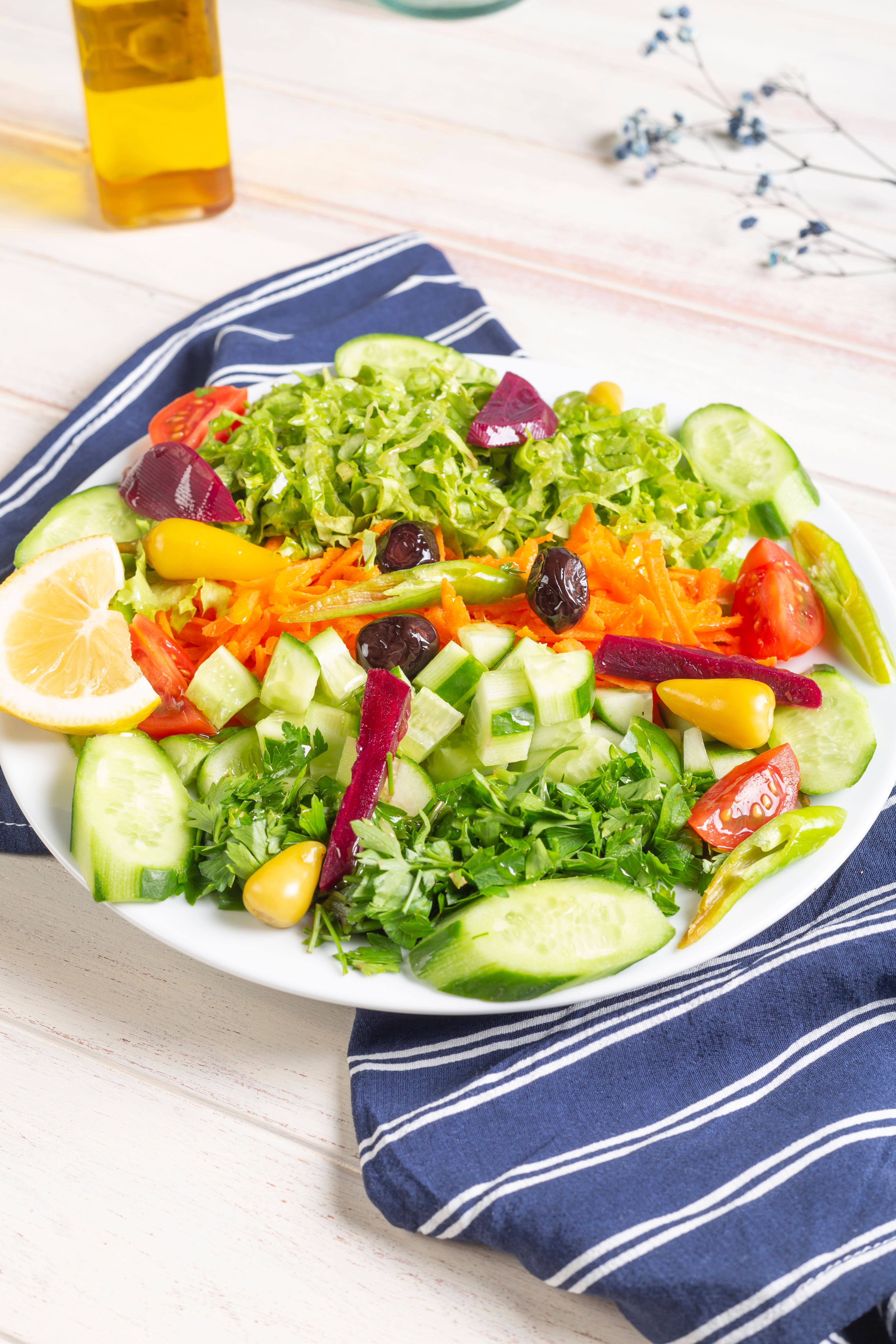 Colorful mixed vegetable salad with cucumbers, tomatoes, and beets on a white plate with a striped cloth.