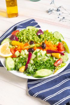 Colorful mixed vegetable salad with cucumbers, tomatoes, and beets on a white plate with a striped cloth.