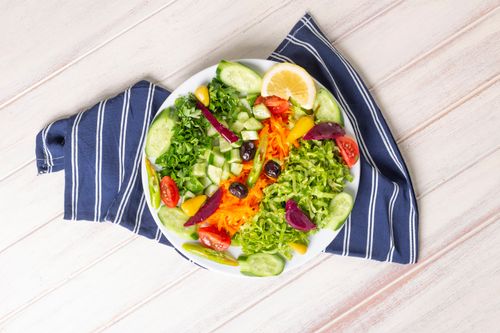 Free A colorful and fresh salad with assorted vegetables, lemon slice, and olives on a plate. Stock Photo