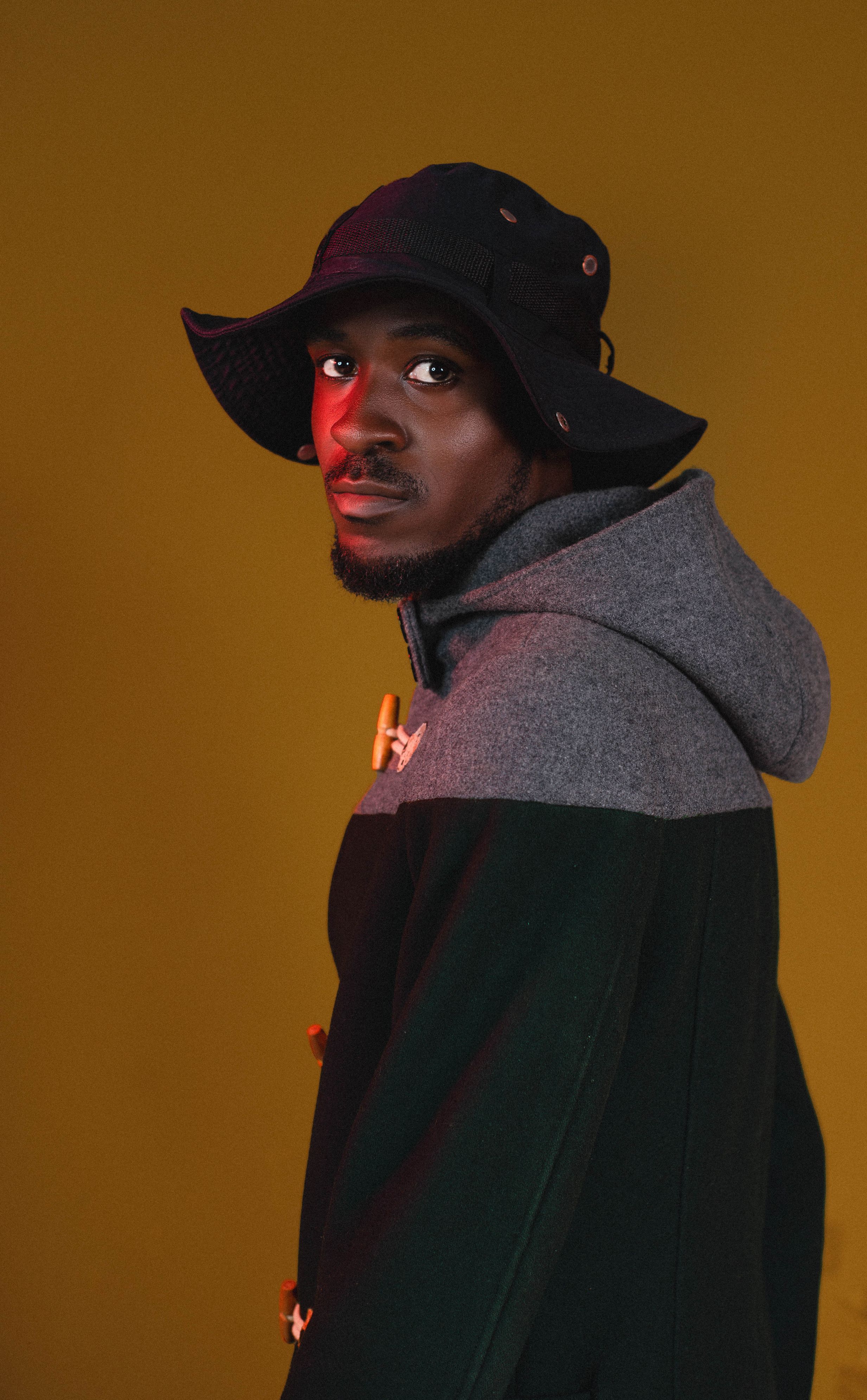 Stylish portrait of a young man wearing a hat and coat against a warm background.
