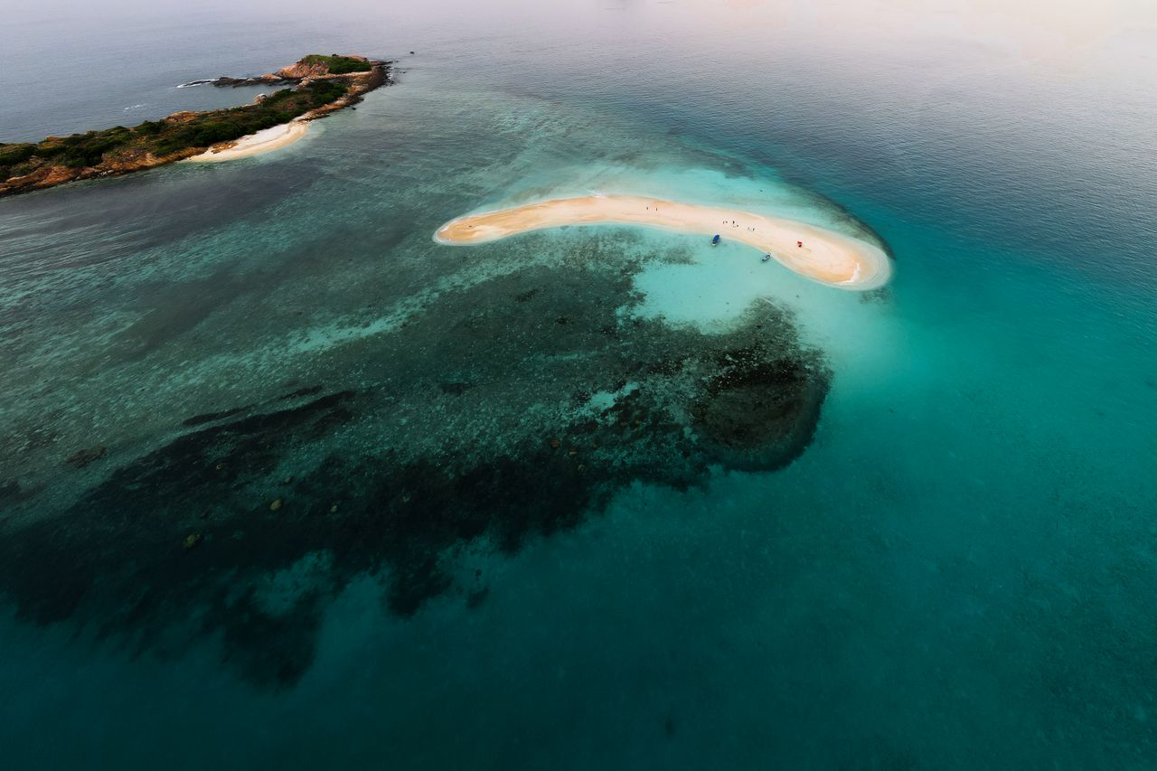 Aerial view of a curved white sandbar surrounded by turquoise reef water