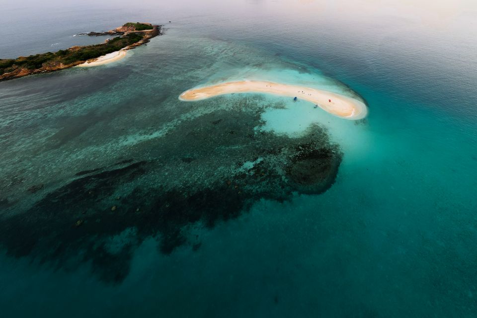 Aerial view of a curved white sandbar surrounded by turquoise reef water
