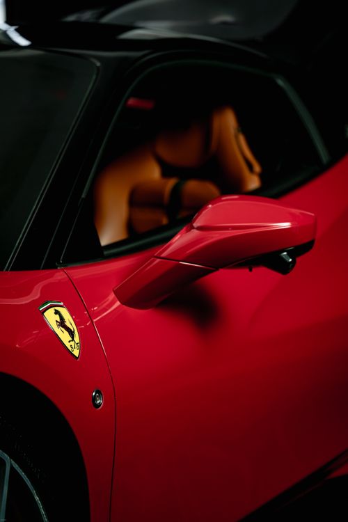 Free Detailed shot of a red luxury sports car, highlighting its sleek design and iconic logo. Stock Photo