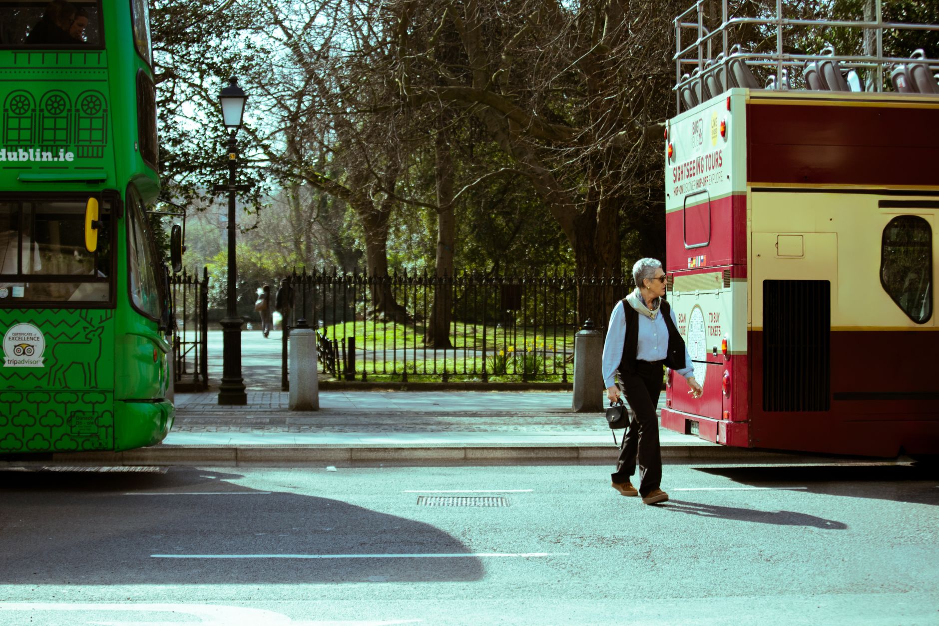 A man walks between two tour buses on a sunny day in Dublin, Ireland, highlighting urban travel vibes.