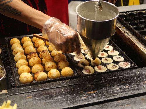 Free Close-up of a vendor preparing traditional takoyaki in a street market in the Philippines, showcasing the cooking process. Stock Photo