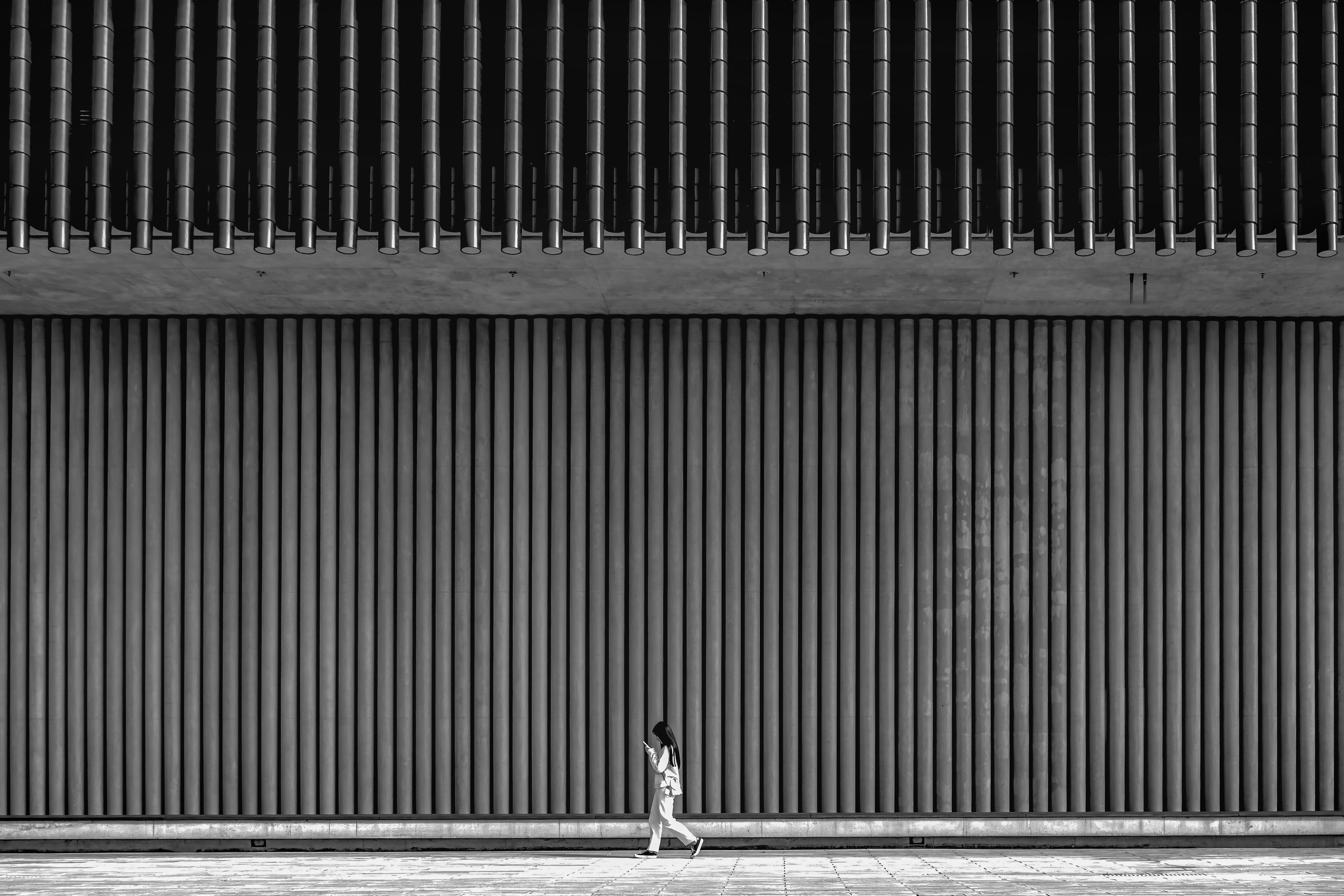 Black and white photo of a woman walking past a modern building facade in Hong Kong.