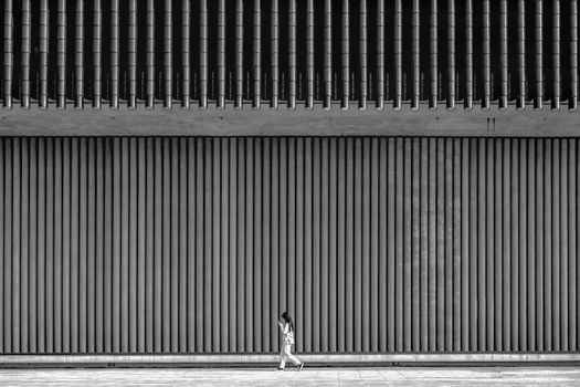 Black and white photo of a woman walking past a modern building facade in Hong Kong.