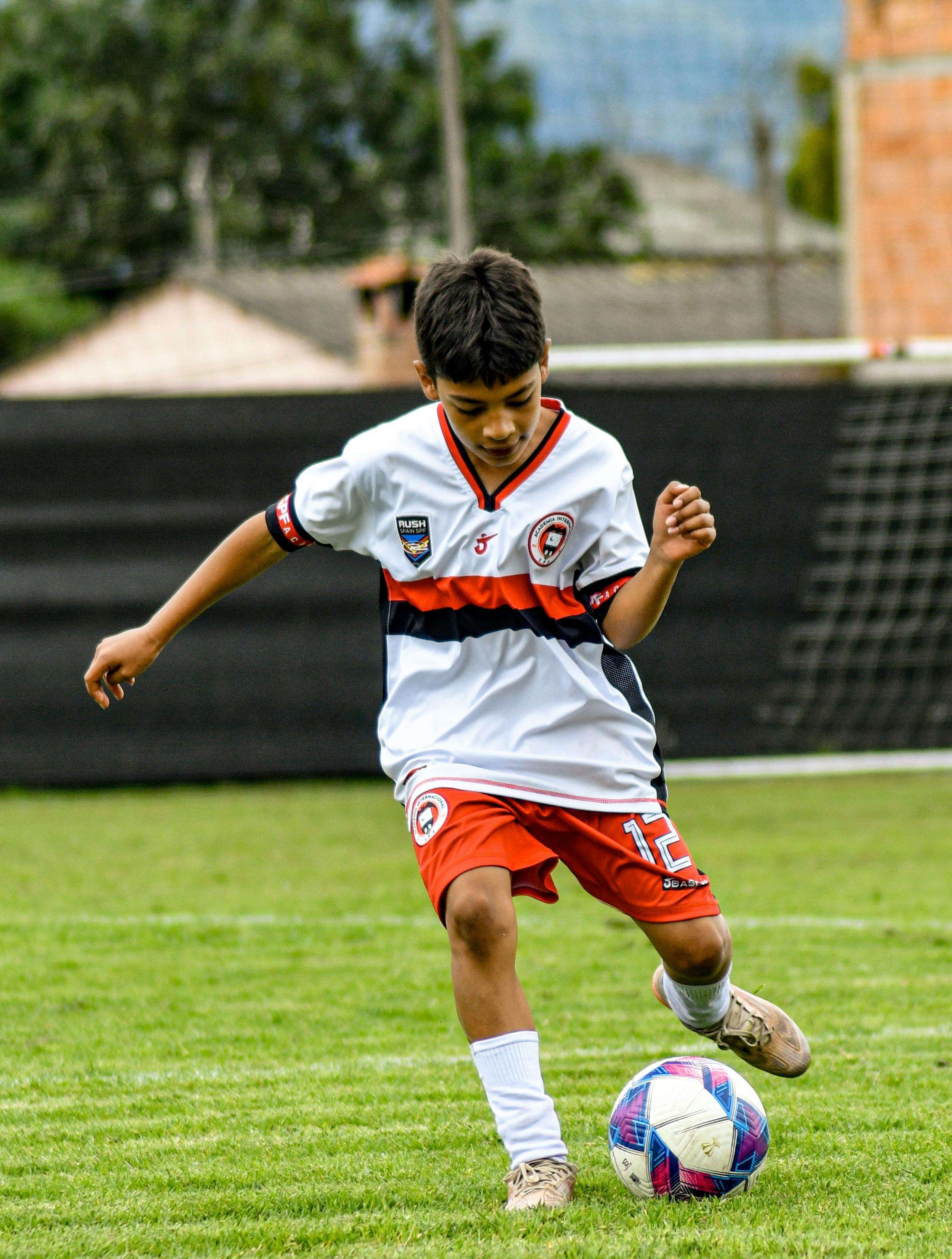 Energetic young boy playing soccer outdoors on a grass field in a team uniform.