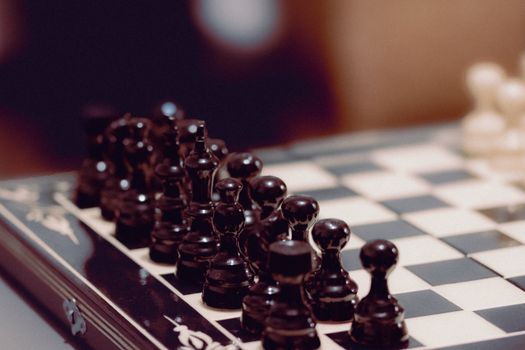 Close-up of black chess pieces aligned on a chessboard, ready for play.