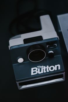 A stylish close-up of a vintage 'The Button' Polaroid camera on a dark background.