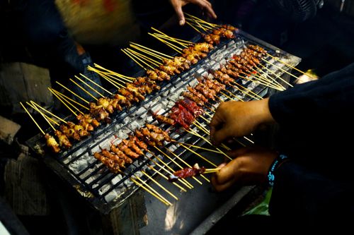 Free Juicy chicken and beef sate skewers grilling over charcoal at a bustling Indonesian night market. Stock Photo