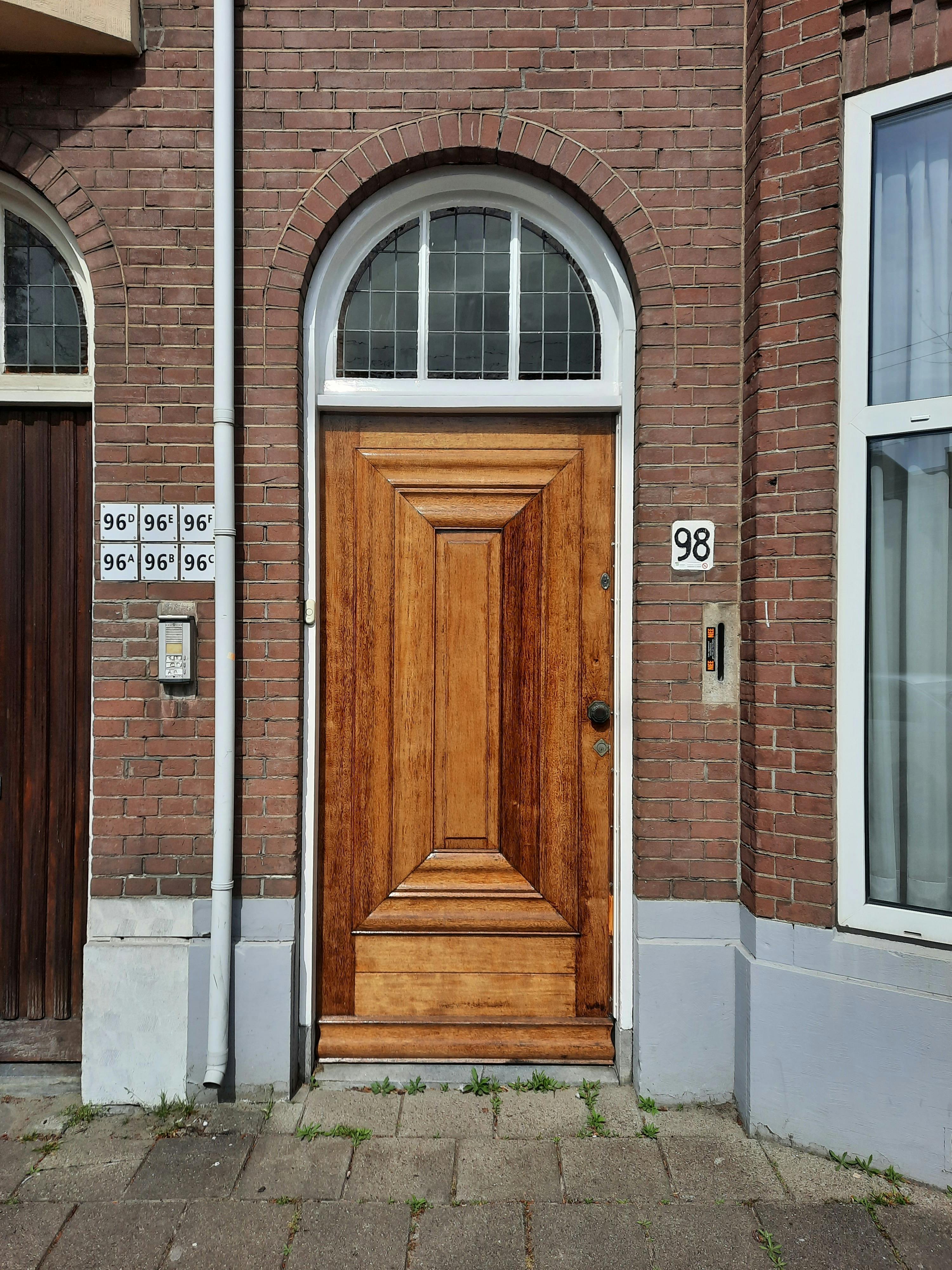 Brown wooden door with arched window in brick facade, Den Haag, Netherlands.