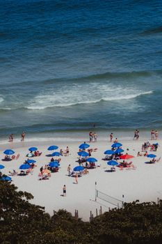 Aerial view of a lively Rio de Janeiro beach with umbrellas and sunbathers enjoying a sunny day.