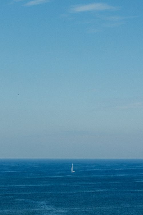 Free A lone sailboat gracefully glides on the calm, expansive ocean under a clear blue sky in Rio de Janeiro, Brazil. Stock Photo