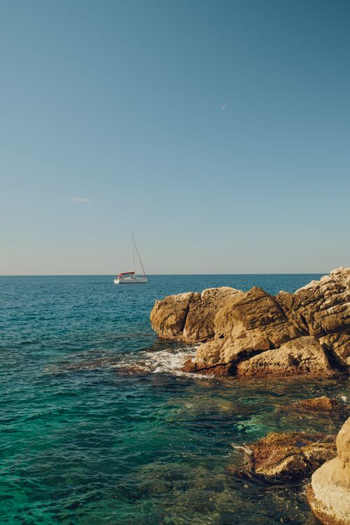 Free A serene view of the Dubrovnik coastline featuring rocky shores and a boat on the Adriatic Sea. Stock Photo